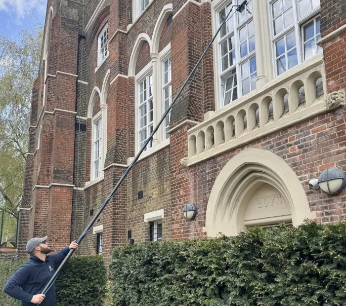 Working the pure water pole across the upper windows of a period house behind a hedge