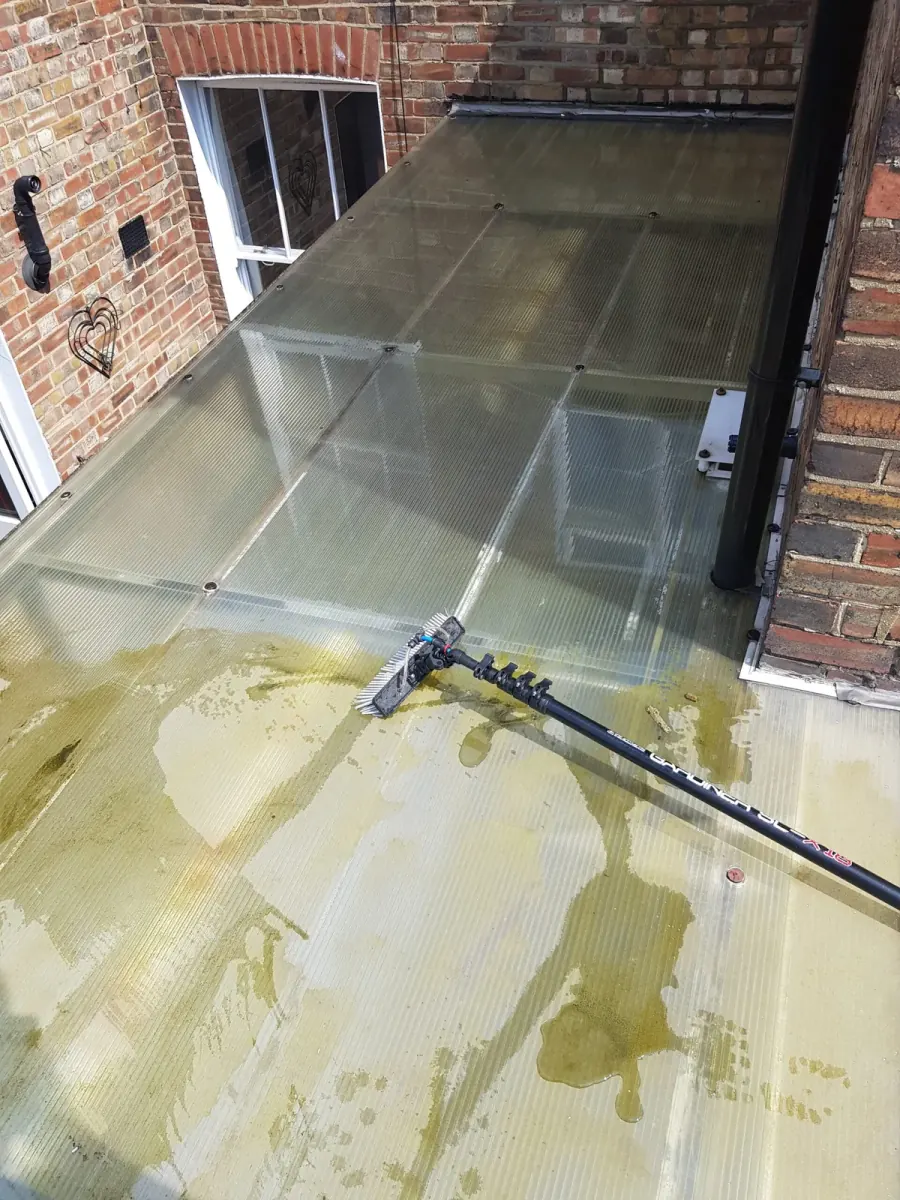 The same glass roof being cleaned with a pole, the dirt lifted and the glass running clear