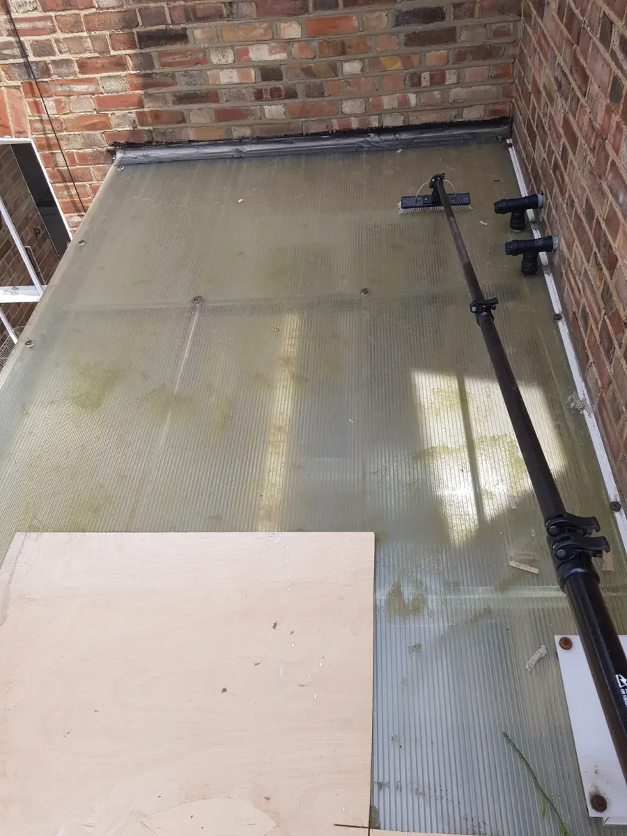 Glass roof between two brick walls before cleaning, dulled with dirt and algae